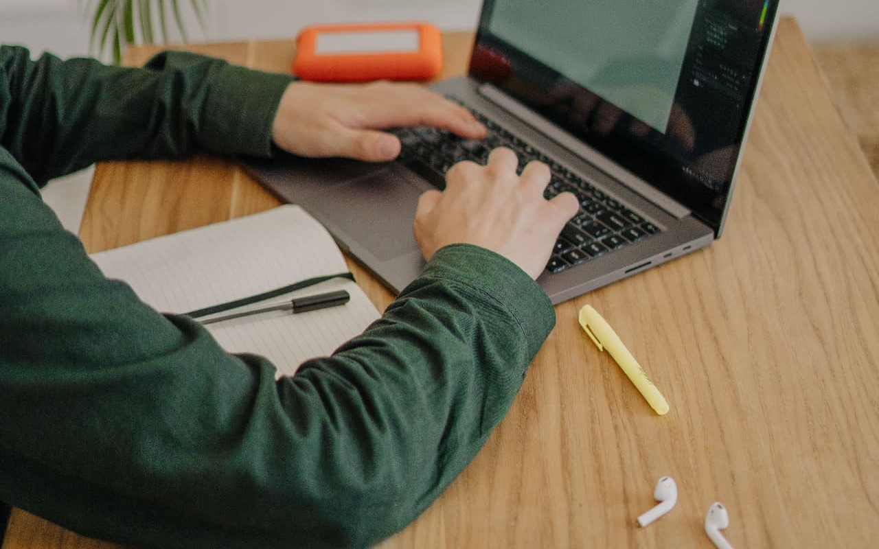 Student studying at a laptop with notebook, tablet and earbuds on a desk